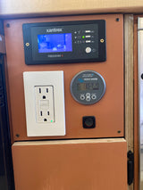 RV rental power control panel: Xantrex inverter, Victron battery monitor showing 13.57V, and a GFCI outlet for off-grid power.