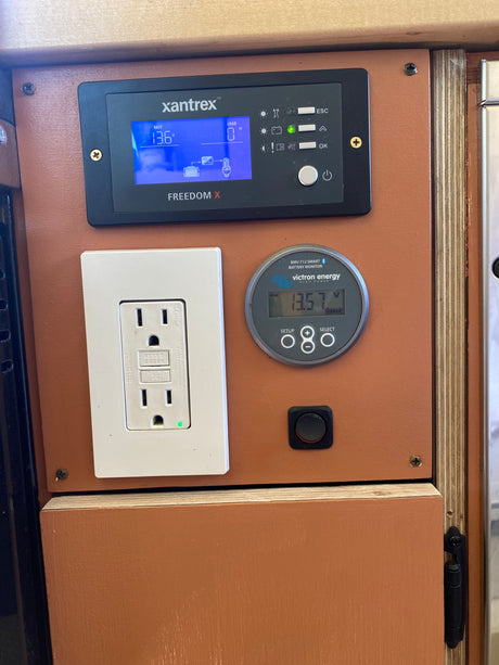 RV rental power control panel: Xantrex inverter, Victron battery monitor showing 13.57V, and a GFCI outlet for off-grid power.