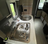 Compact RV rental kitchen: two-burner stove, sink, and counter visible, ready for travel cooking.