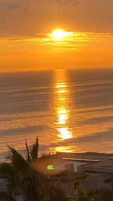 Golden sunset over ocean & coast, ideal for an RV rental vacation. Features palm trees, homes, and sun's path.