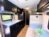 RV rental interior: modern kitchen with black cabinets, white counters, dining area, and cozy bench seating.