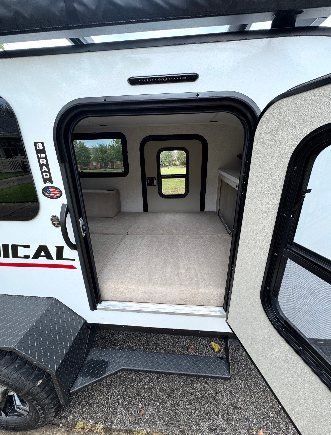 Inside a white RV rental camper with its door open, revealing a cozy interior bed, small windows, and entry steps.