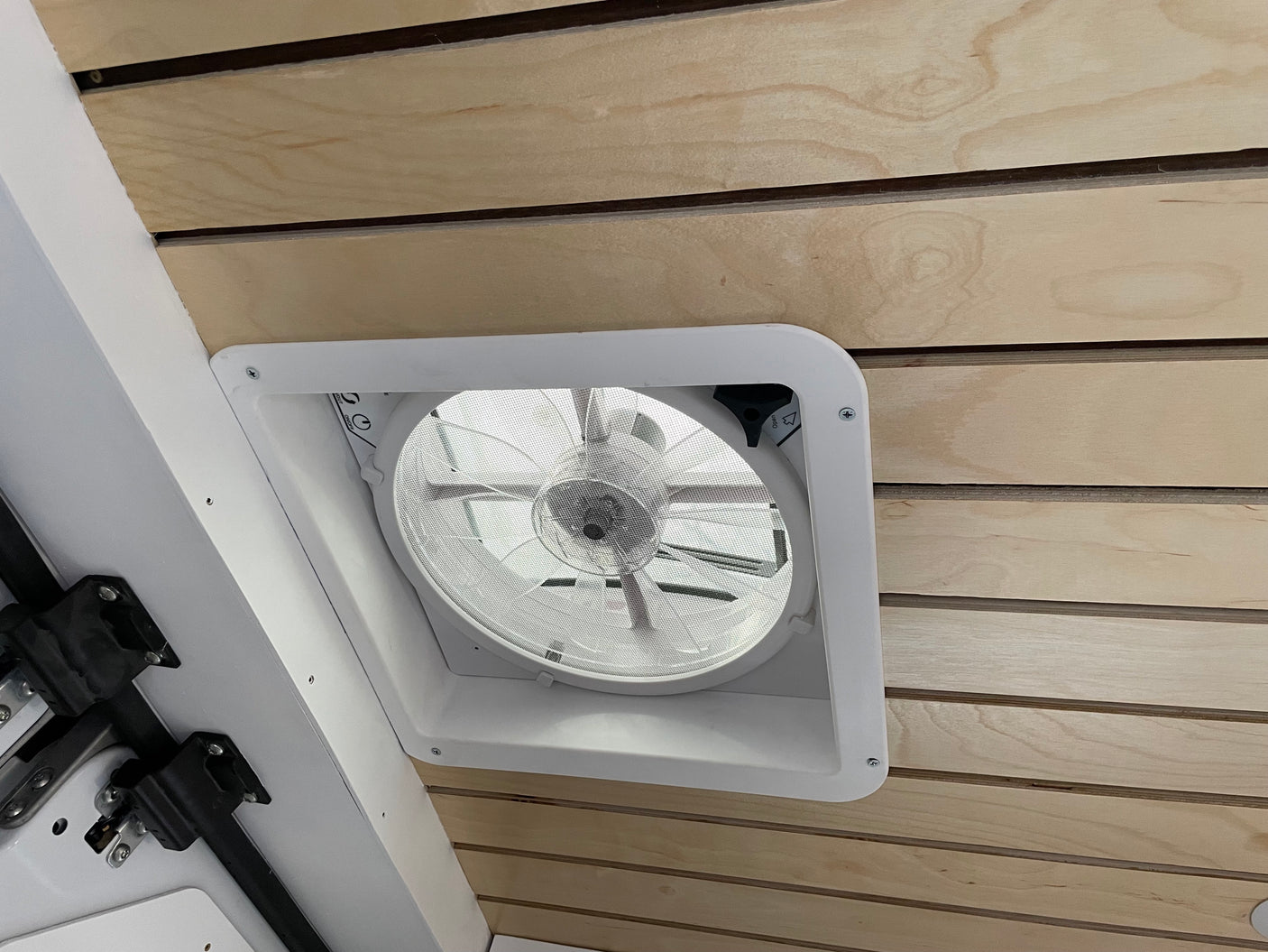 Interior view of an RV rental ceiling with a white fan/vent and light wood planks, enhancing comfort for travelers.