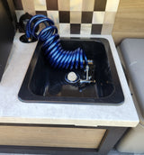 Compact RV rental utility sink with blue coiled shower hose & faucet, perfect for a camper's outdoor washing station.
