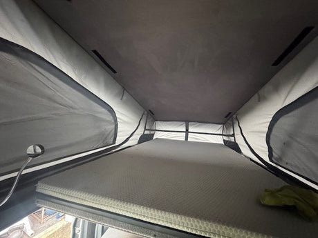 Inside this rv rental pop-top camper: a raised sleeping area with a textured mattress, light fabric walls, and mesh windows.