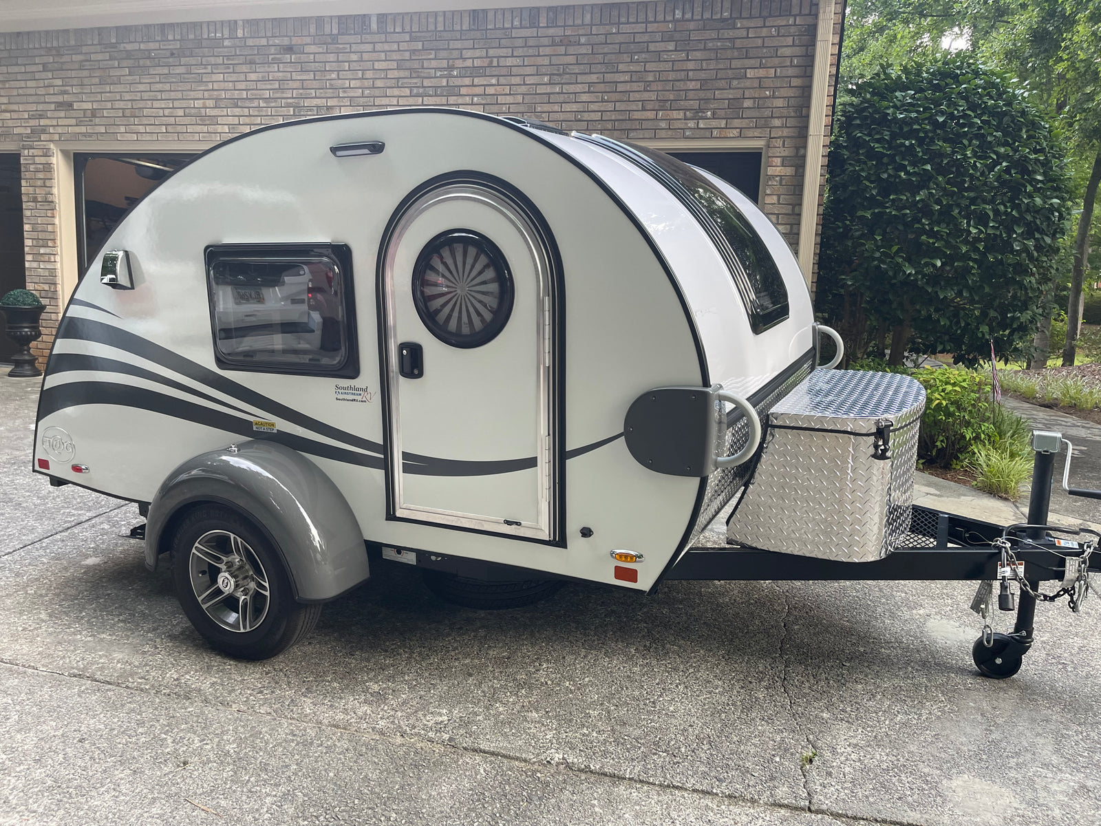 This white teardrop RV rental, with a distinct rounded design and diamond plate storage box, is ready for your next trip.