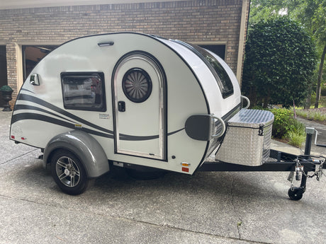 This white teardrop RV rental, with a distinct rounded design and diamond plate storage box, is ready for your next trip.