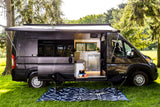 RV rental: This fully-equipped camper van features an open side door revealing a modern kitchen, extended awning, and outdoor seating.