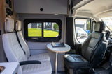 Cozy RV rental interior with seating, a table, and chess set, offering a view of a house outside.