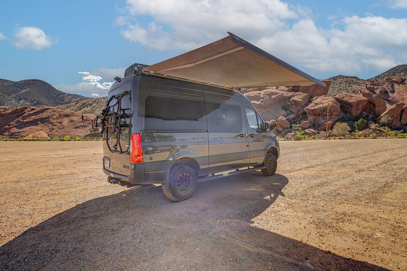 Mercedes Sprinter RV rental with awning & bike rack, parked in a scenic red rock desert. Ready for outdoor adventures.
