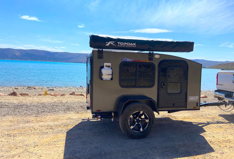 An off-grid Hiker Trailer RV rental parked lakeside, ideal for scenic outdoor camping adventures.