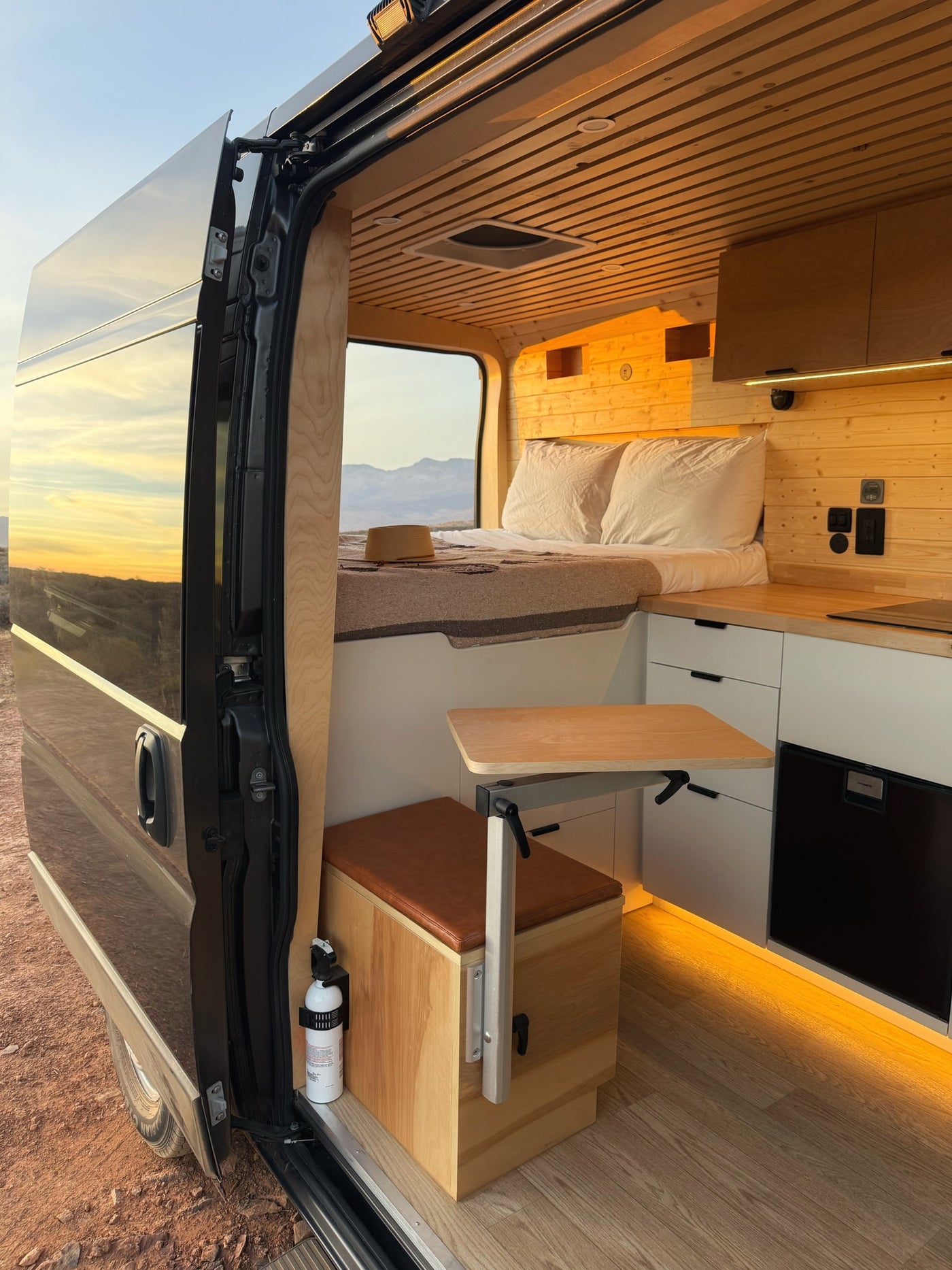 Inside an RV rental: a modern camper van with cozy wood interior, bed, kitchenette, and a flexible dining table, featuring a sunset view. — photo 4