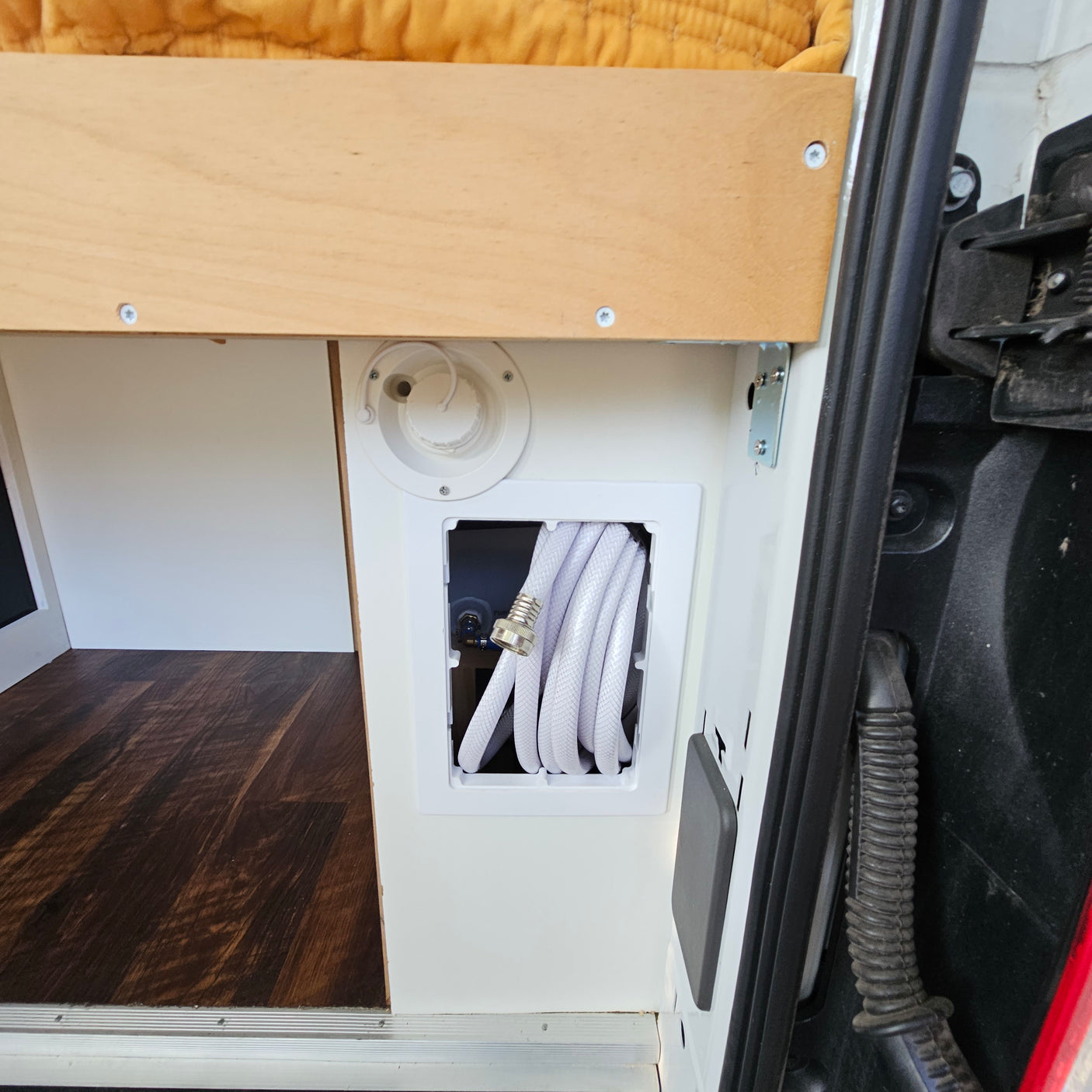 RV rental interior: a white panel with a water fill port and a coiled outdoor shower hose neatly stored.