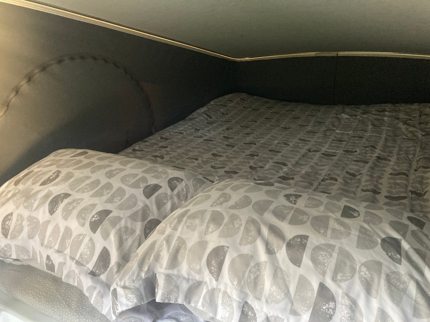 Cozy bed inside an RV rental, featuring soft grey patterned bedding and pillows, offering a comfortable sleeping area. — photo 5