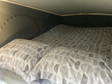 Cozy bed inside an RV rental, featuring soft grey patterned bedding and pillows, offering a comfortable sleeping area.