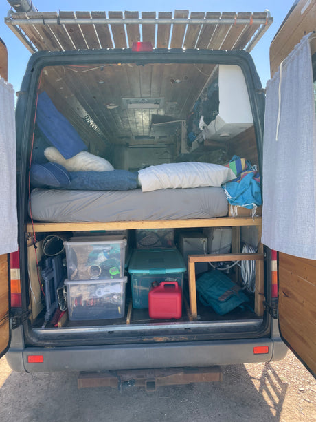 Rear view of an RV rental's custom camper van interior, featuring a bed, organized storage, and a roof rack.