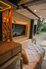 Stylish rv rental interior: custom wood panels, warm ambient lighting, cozy bench with blanket, and a large window view.