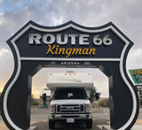 Front view of an RV rental under the large black and white Route 66 Kingman archway in Arizona. Ready for adventure!