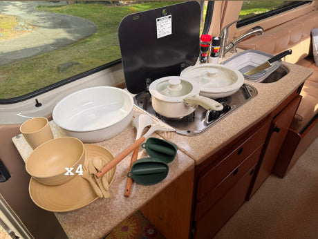 Inside an RV rental: a compact kitchen featuring a stove, sink, cookware, and dinnerware, perfect for travel and camping meals.