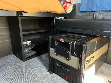 RV rental interior: smart setup includes a raised bed, dark storage shelves, and an ARB ZERO portable fridge/freezer.