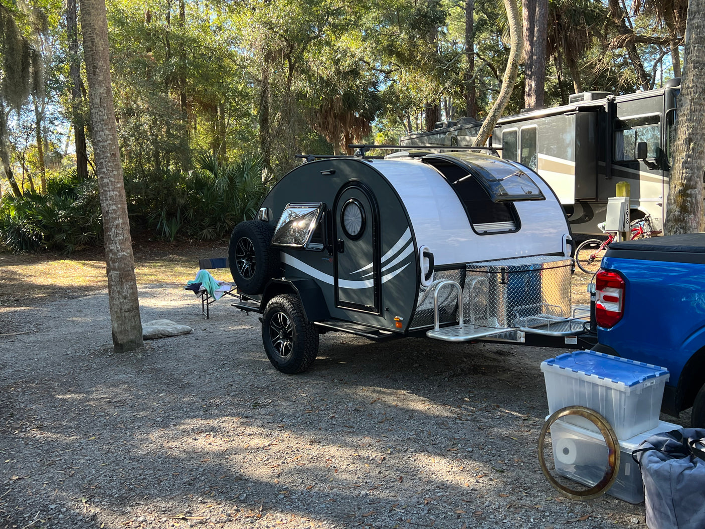Compact teardrop travel trailer and blue pickup truck at a shaded campground, ideal for an rv rental getaway.