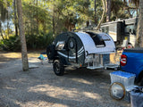 Compact teardrop travel trailer and blue pickup truck at a shaded campground, ideal for an rv rental getaway.