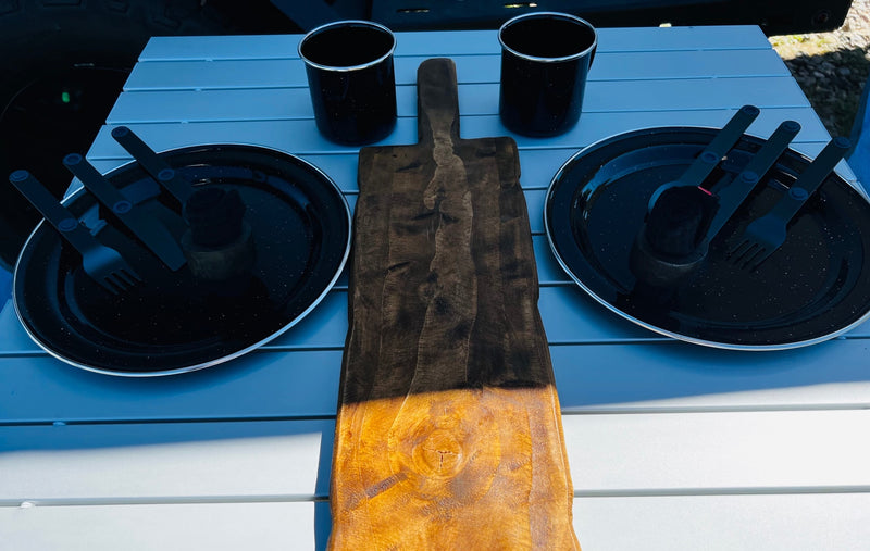 RV rental camping gear: Black plates, mugs, cutlery, and a rustic cutting board neatly arranged on an outdoor table. — photo 11