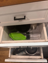 Neat RV rental kitchen storage: green colander, blender cup, plates, pot, and knife in drawers.