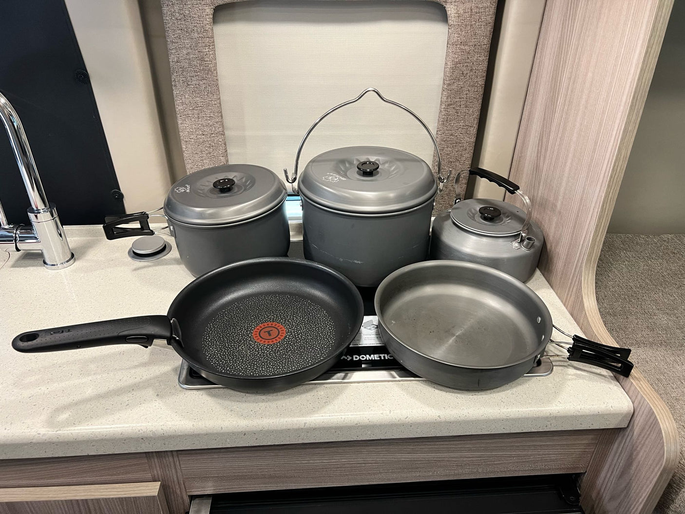 RV rental kitchen showing gray GSI camping pots, pans, kettle, and a T-fal skillet on a Dometic stove.