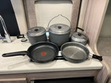 RV rental kitchen showing gray GSI camping pots, pans, kettle, and a T-fal skillet on a Dometic stove.
