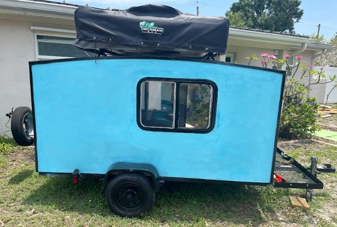 Rear view of a light blue DIY mini camper with an Ironman rooftop tent, available for RV rental.
