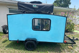 Rear view of a light blue DIY mini camper with an Ironman rooftop tent, available for RV rental.