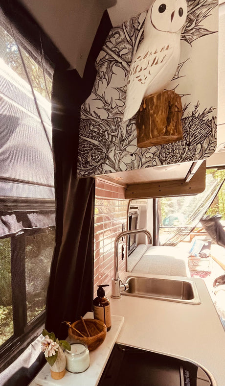 RV rental's custom kitchenette: pink tile backsplash, steel sink, and a white owl on thistle wallpaper.