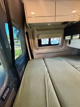 An rv rental's cozy rear interior features two beds with green covers, windows, and overhead storage.