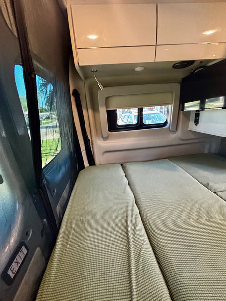 An rv rental's cozy rear interior features two beds with green covers, windows, and overhead storage.