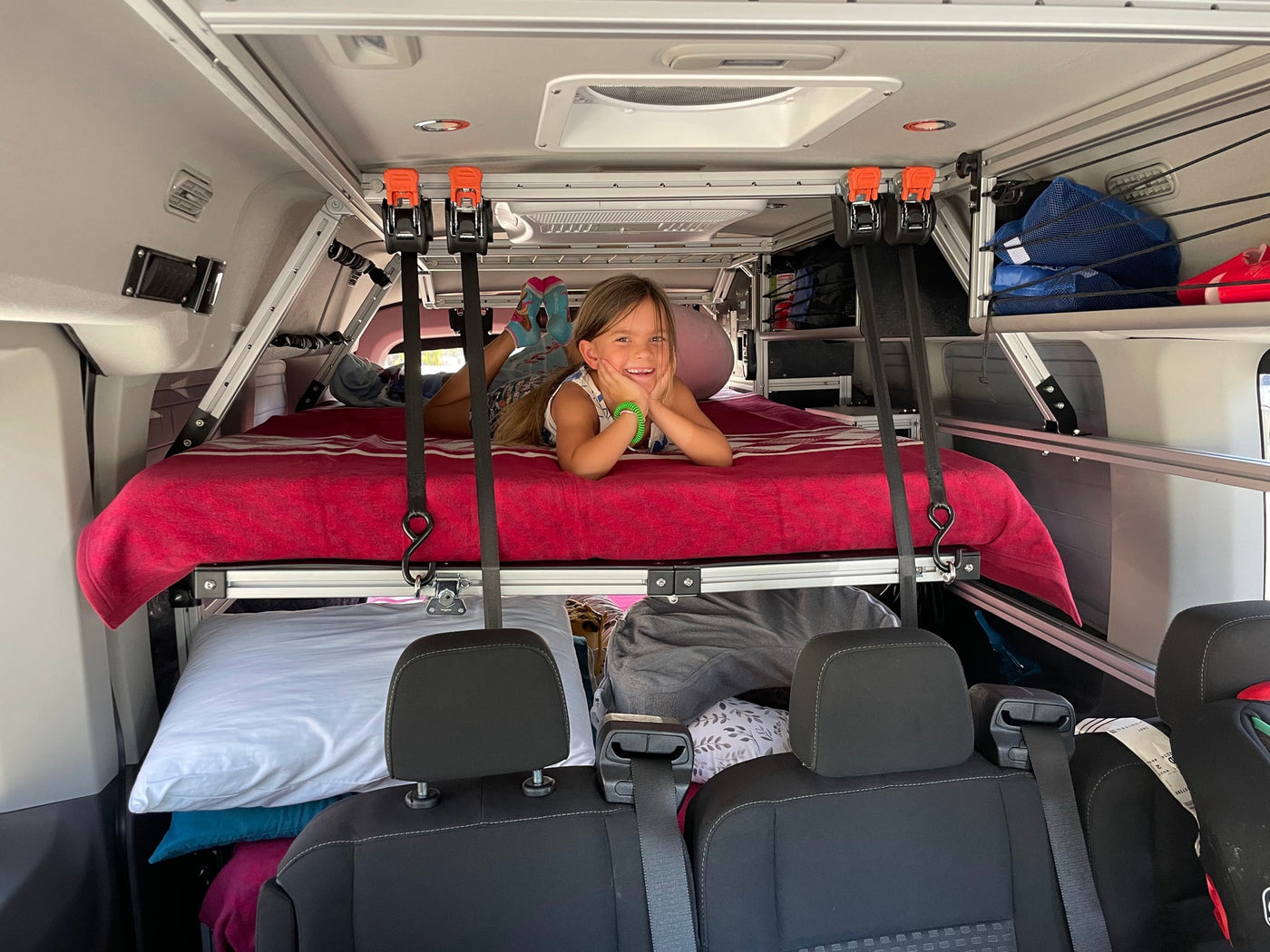 RV rental fun! A happy child enjoys the elevated bed in a custom camper van, with practical storage below. — photo 13
