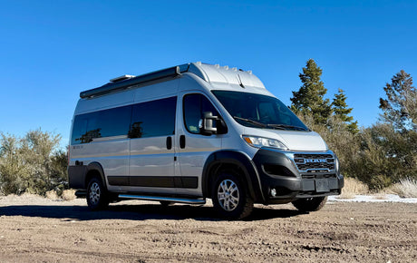 Silver Integra Ethos Class B camper van, a perfect rv rental for adventure, parked on a dirt path under a clear blue sky.