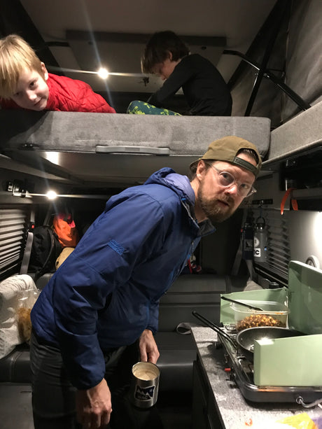 Cozy RV rental interior with dad cooking, kids on bunk. Family enjoying travel.