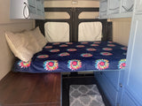 Inside a custom RV rental: cozy bed with floral blanket, overhead storage, and under-bed drawers. Perfect for adventure!