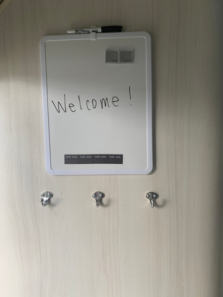 RV rental interior featuring a 'Welcome!' whiteboard, marker, and three hooks on a light wood-grain wall.