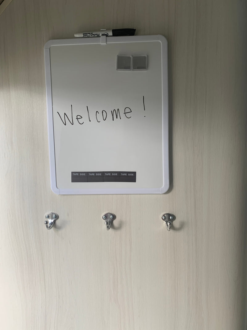 RV rental interior featuring a 'Welcome!' whiteboard, marker, and three hooks on a light wood-grain wall. — photo 15