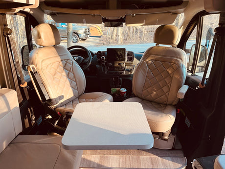RV rental interior: Swivel seats, table, and dashboard tech setup. Scenic outdoor view with truck, tent, and nature.