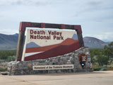 Rustic Death Valley National Park sign on stone base. Desert mountains in background, great for an RV rental adventure.
