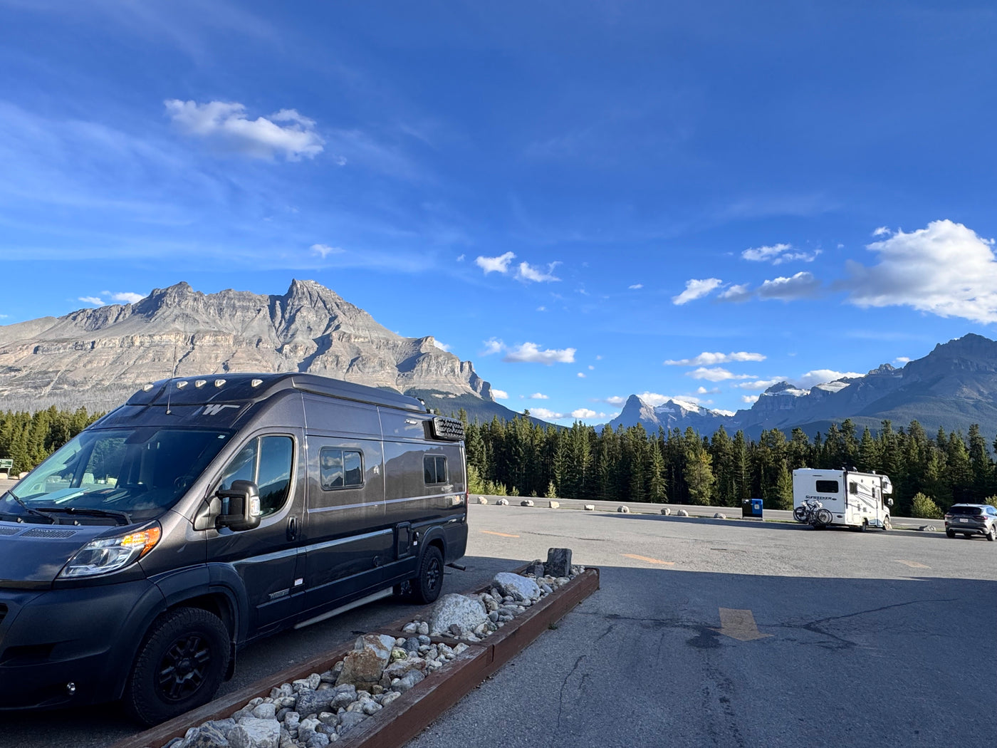 An RV rental (dark gray camper van) parked in a scenic mountain setting, with majestic peaks, forests, and a blue sky. — photo 17