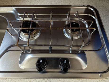 RV rental's compact stainless steel two-burner cooktop with integrated sink, ready for travel adventures.