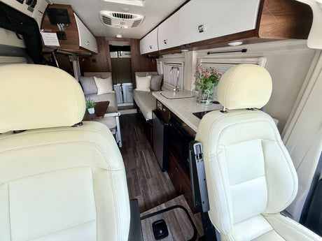View from the front seats of a modern RV rental, featuring a compact kitchen, cozy seating, and clean interior.
