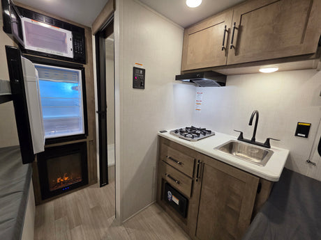 Cozy RV rental interior showcasing a well-equipped kitchenette with sink, cooktop, microwave, fridge, and electric fireplace.