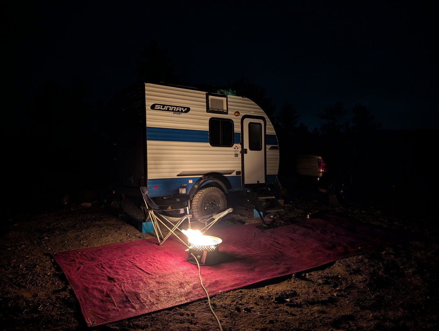 Night camping with an rv rental teardrop trailer and a glowing propane campfire on a red mat. Peaceful outdoor adventure.