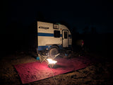 Night camping with an rv rental teardrop trailer and a glowing propane campfire on a red mat. Peaceful outdoor adventure.