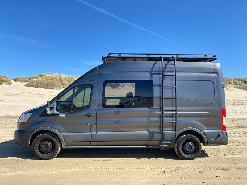A dark gray camper van, perfect for an RV rental, parked on a sunny sandy beach with tall dunes under a clear blue sky. — photo 1